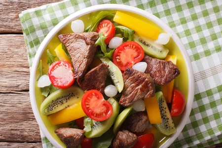 salad of roast beef, kiwi fruit, tomatoes, peppers and arugula close-up on a table in a bowl. horizontal view from aboveの写真素材