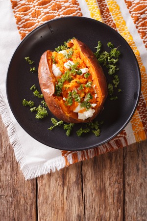 Whole sweet potato baked with cheese, spices and parsley close-up on a black plate on the table. vertical view from above
の写真素材