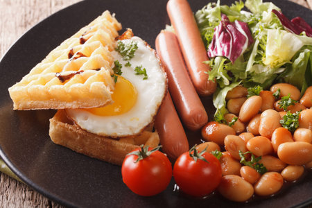 Delicious breakfast: fried egg, waffles, sausages, beans and salad close-up on a plate. horizontal