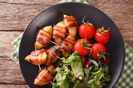 Fried potatoes wrapped in bacon and fresh salad close-up on a plate. Horizontal view from aboveの写真素材