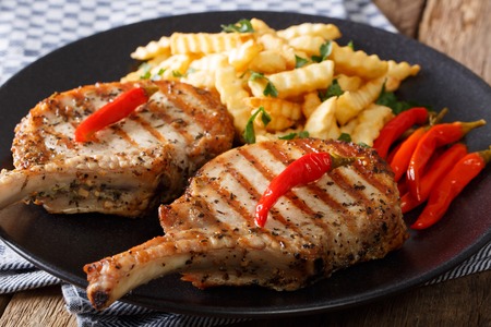 Grilled pork chop with bone, chili and fries close-up on plate on table. horizontalの写真素材