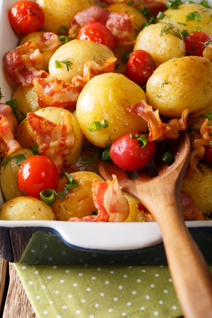 Hot new potatoes baked with bacon and tomatoes close-up in a baking dish. verticalの写真素材