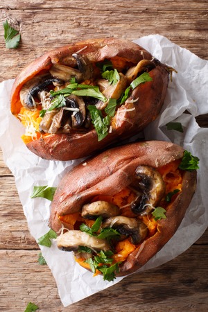 Organic baked sweet potato with mushrooms, herbs and cheese close-up on parchment on the table. vertical top view from aboveの写真素材
