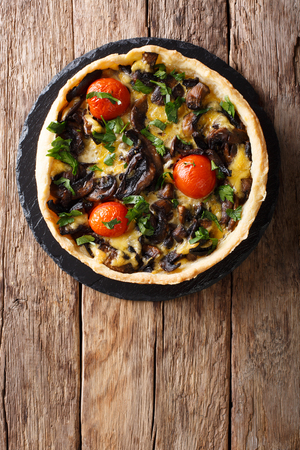 Freshly baked mushroom pie with cheese, parsley and tomatoes close-up on the table. vertical top view from aboveの写真素材