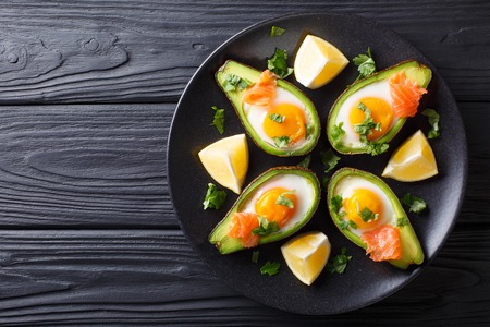 Baked avocado with egg, smoked salmon and greens close-up on a plate on a table. horizontal top view from above background
の写真素材