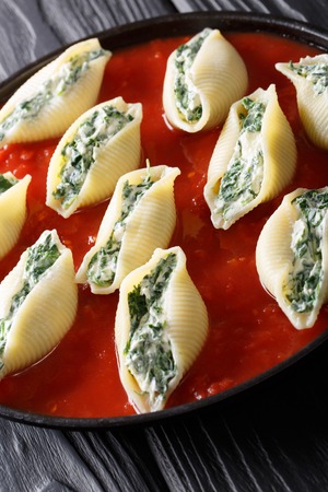 Delicious conchiglioni pasta stuffed with spinach and ricotta cheese with tomato sauce close-up on a plate. vertical
の写真素材