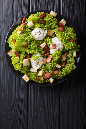 Gourmet salad Lyonnaise with lettuce, crispy bacon, croutons and poached eggs close-up on a plate on the table. Vertical top view from aboveの写真素材