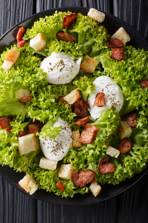 French salad Lyonnaise with lettuce, crispy bacon, croutons and poached eggs close-up on a plate on the table. Vertical top view from above
の写真素材