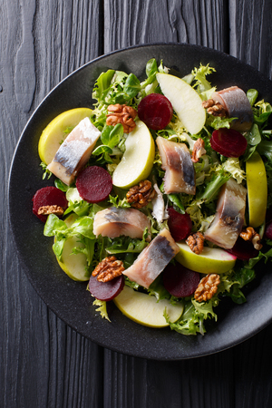 Freshly prepared mackerel salad with apples, walnuts, beets and mix lettuce close-up on a black plate on the table. Vertical top view from above
の写真素材