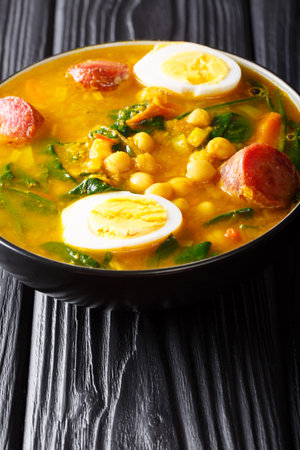 Spanish Potaje de vigilia con garbanzos spinach with chickpeas, sausages and eggs close-up in a bowl on the table. verticalの写真素材