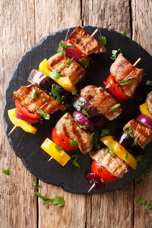 Juicy grilled kebabs of pork with tomatoes, pepper, onions and eggplants close-up on a slate plate on a table. Vertical top view from above
の写真素材