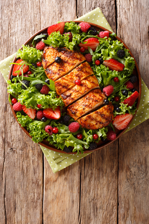 Organic salad of grilled chicken breast with fresh berries, lettuce and arugula closeup on plate on table. Vertical top view from aboveの写真素材