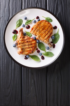 Grilled pork steak with blueberry sauce and spinach close-up on a plate. Vertical top view from aboveの写真素材