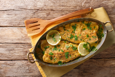 Spicy baked trout fillets with garlic butter sauce, lemon and parsley close-up in a copper frying pan on a table. Horizontal top view from aboveの写真素材