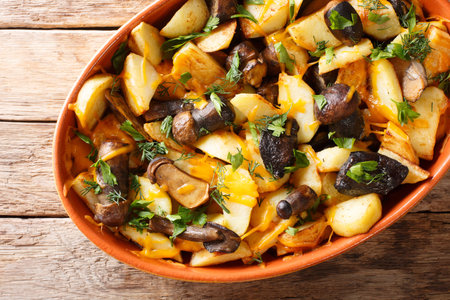 Baked potato wedges with forest mushrooms, cheddar cheese and herbs close-up in a baking dish on a...