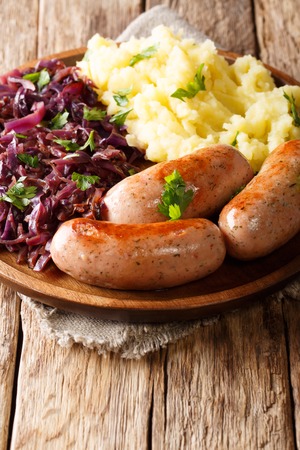 Served mashed potatoes with stewed red cabbage and fried sausages close-up on a plate on a table. verticalの写真素材
