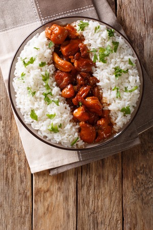 Stewed Bourbon chicken in sauce with whiskey, sugar, ginger and soy, served with rice on a plate on the table. Vertical top view from aboveの写真素材