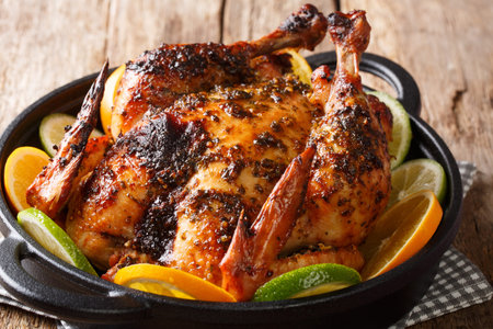 Citrus whole baked chicken served with fresh oranges and limes close-up in a frying pan on the...