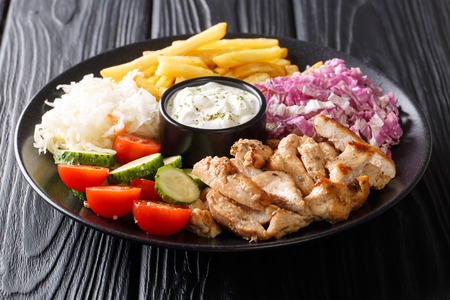 Doner kebab on a plate with french fries, salad and sauce close-up on a wooden table. horizontalの写真素材