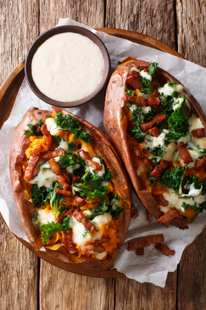 Delicious whole baked sweet potato with fresh kale, bacon and cheese sauce close-up on a plate on the table. Vertical top view from aboveの写真素材