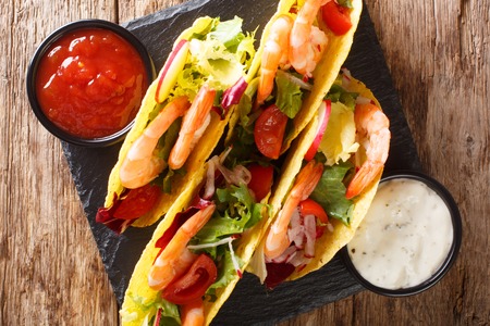 Delicious Mexican tacos with shrimps and vegetables close-up on the table served with sauces. horizontal top view from aboveの写真素材