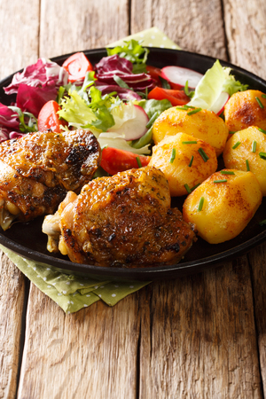 Delicious chicken thighs served with young potatoes and fresh salad close-up on a plate on the table. verticalの写真素材