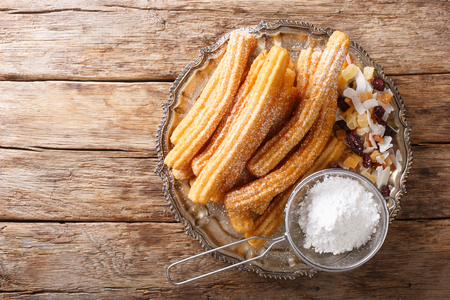 Freshly made hot churros with powdered sugar and candied fruits close-up on the table. horizontal top view from aboveの写真素材