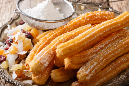 Freshly made hot churros with powdered sugar and candied fruits close-up on the table. horizontalの写真素材