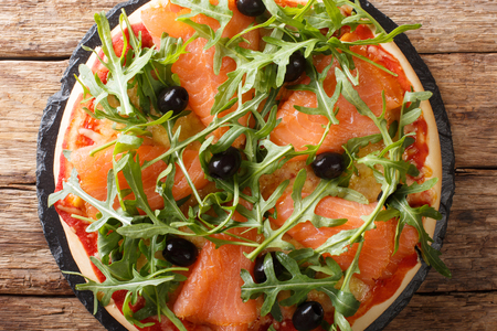 Salmon pizza with fresh arugula, black olives and cheese closeup on the table. horizontal top view from aboveの写真素材