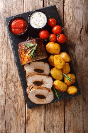 Delicious pork tenderloin with prunes served with new potatoes and sauces close-up on the table. Vertical top view from aboveの写真素材
