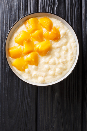 Sweet tapioca pudding with coconut milk and fresh mango close-up in a bowl on the table. Vertical top view from aboveの写真素材