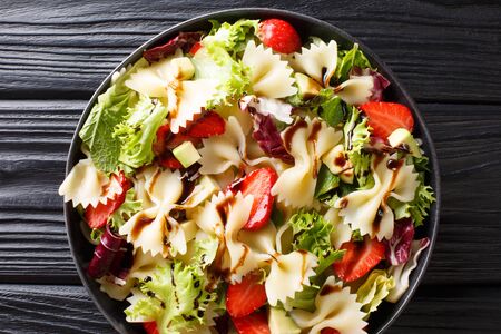 Farfalle pasta with avocado, strawberries, mix lettuce and balsamic dressing close-up on a plate on the table. horizontal top view from aboveの写真素材