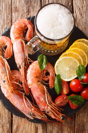 foamy beer with tasty shrimps, lemon and tomatoes close-up on a slate board on the table. Vertical top view from aboveの写真素材