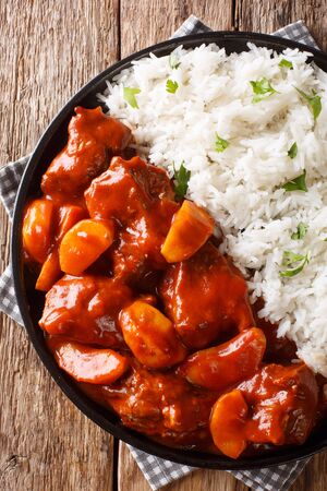 Serving of beef stew with apples in tomato sauce with rice side dish close-up on a plate on the table. Vertical top view from aboveの写真素材