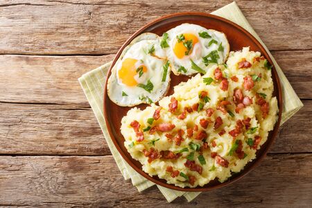 Freshly cooked mashed potatoes with bacon and parsley served with fried eggs close-up on a plate on the table. Horizontal top view from above
の写真素材