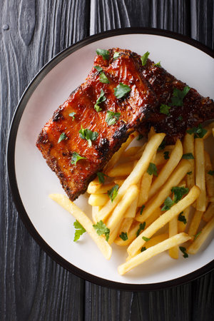 Grilled short ribs served with french fries close-up on a plate on the table. Vertical top view from above