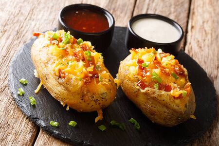 Fragrant stuffed potato with cheese, green onions and bacon served with ketchup and sour cream close-up on the table.の写真素材