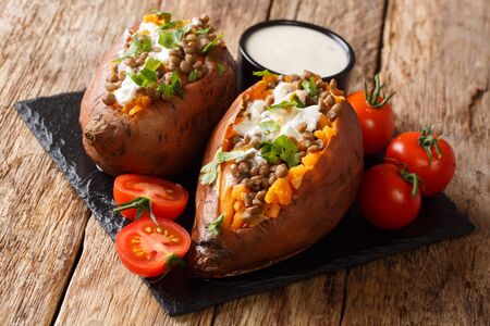 Vegetarian menu baked sweet potato with lentils served with sour cream and tomatoes close-up on a slate board on the table. horizontalの写真素材