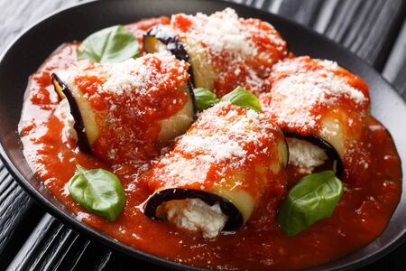 eggplant rolls stuffed with ricotta and baked in tomato sauce and served with parmesan and basil close-up in a plate on the table. horizontal
の写真素材