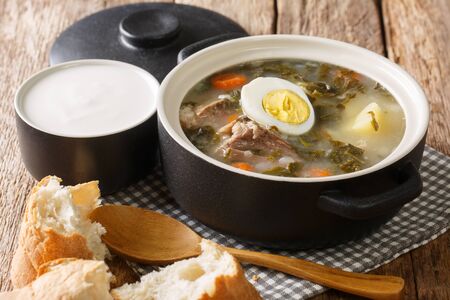 Tasty traditional green borscht made of sorrel, vegetables, eggs, meat with bread and sour cream close-up on the table. horizontal
の写真素材