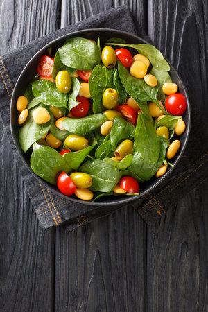 Fresh salad of spinach, lupine beans, tomatoes and olives close-up in a plate on the table. vertical top view from aboveの写真素材