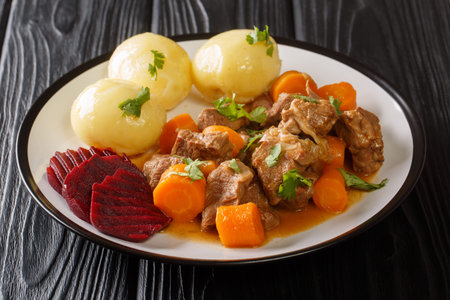 Swedish traditional beef kalops garnished with boiled potatoes and pickled beets close-up in a plate...