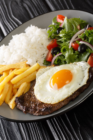 Bitoque is a traditional Portuguese dish, which consists of grilled beef steak with fries, rice, various salads and topped with an egg closeup in the plate on the table. Verticalの写真素材