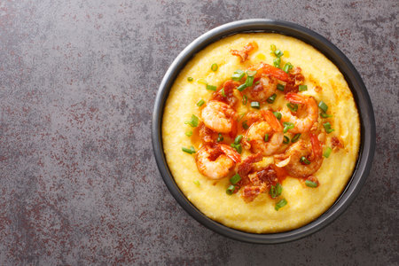 Homemade shrimp and grits with smoked bacon, onions and cheese in a black bowl on a dark concrete background. american cuisine. Horizontal top view from aboveの写真素材