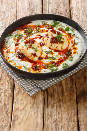 C?lb?r is a Turkish egg dish reminiscent of a poached egg. prepared with yoghurt, garlic served with melted butter soaked in Aleppo pepper closeup in the plate on the wooden table. Verticalの写真素材