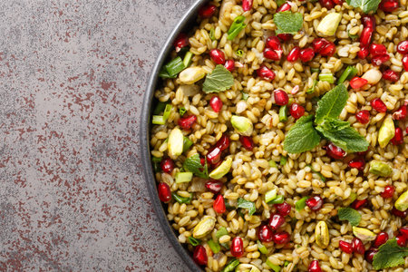 Boiled freekeh with pomegranate, nuts and herbs close-up in a plate on the table. horizontal top...
