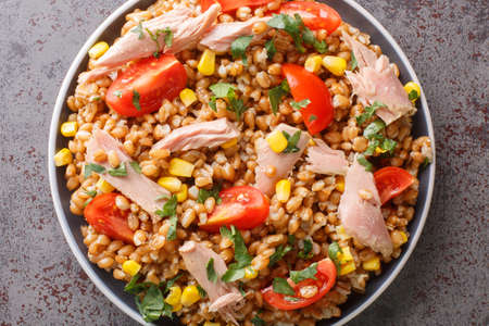 Fresh salad prepared with spelt, tuna, corn, tomatoes and herbs close-up in a plate on the table. horizontal top view from aboveの写真素材