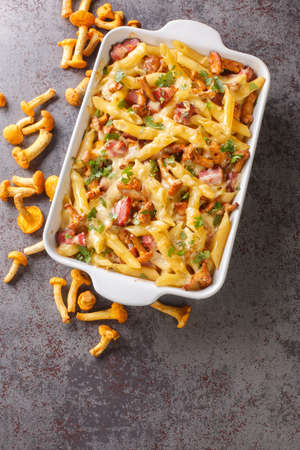 Gratin prepared from penne pasta with chanterelle mushrooms, meat and cheese close-up in a ceramic baking dish on the table. vertical top view from aboveの写真素材