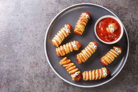Funny sausage mummies in dough with ketchup for the Halloween party. Children's food closeup in the plate on the table. Horizontal top view from aboveの写真素材