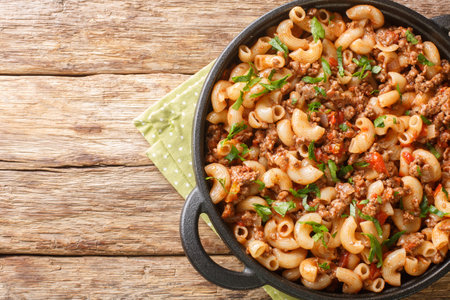 Hamburger Macaroni with vegetables and cheese closeup in the pan on the wooden table. Horizontal top view from aboveの写真素材